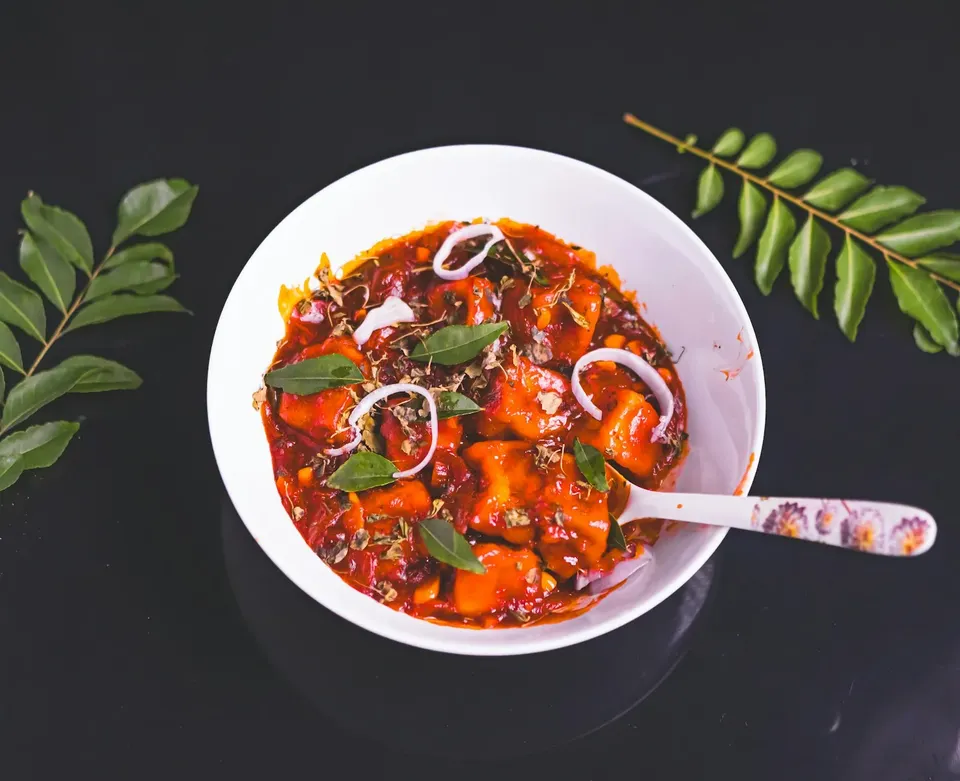 Crispy chilli paneer in a white bowl with spring onions
