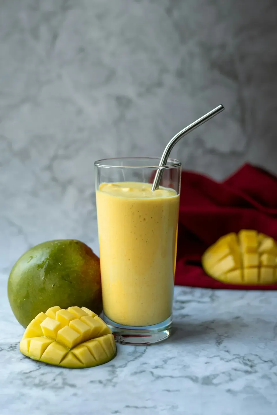 A glass of mango lassi next to a sliced mango