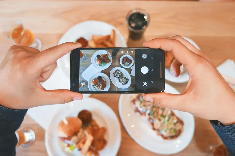 Hands photographing a table of food with a phone